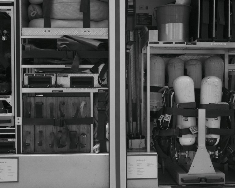 Black and white photo of firetruck equipment and rescue gear neatly organized in compartments.