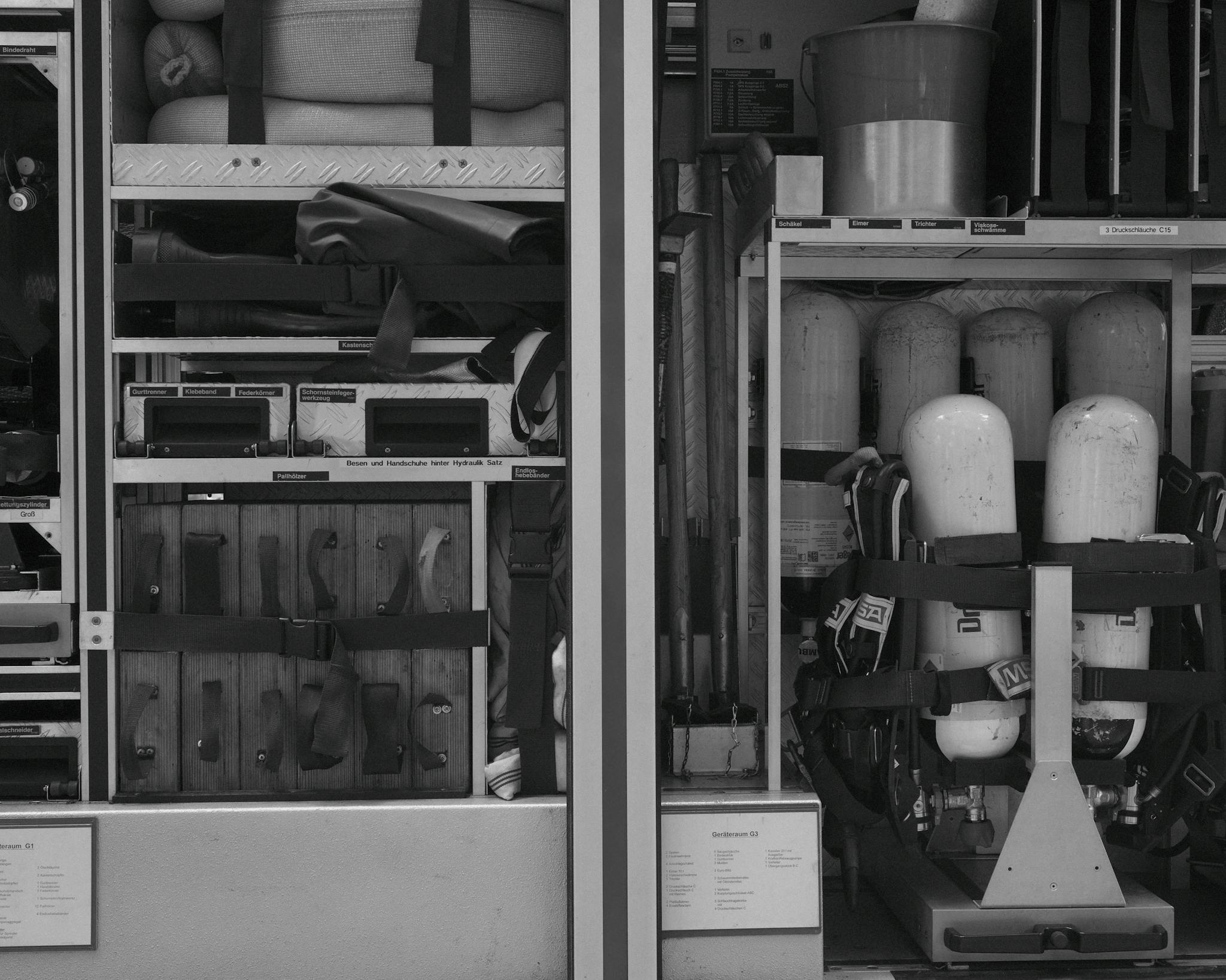 Black and white photo of firetruck equipment and rescue gear neatly organized in compartments.