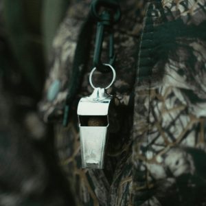 Close-up of a shiny silver whistle hanging against a camouflage-patterned fabric background.