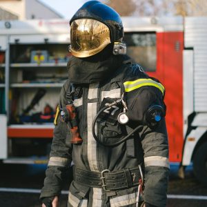 Firefighter in full protective gear standing beside a fire truck during daylight.