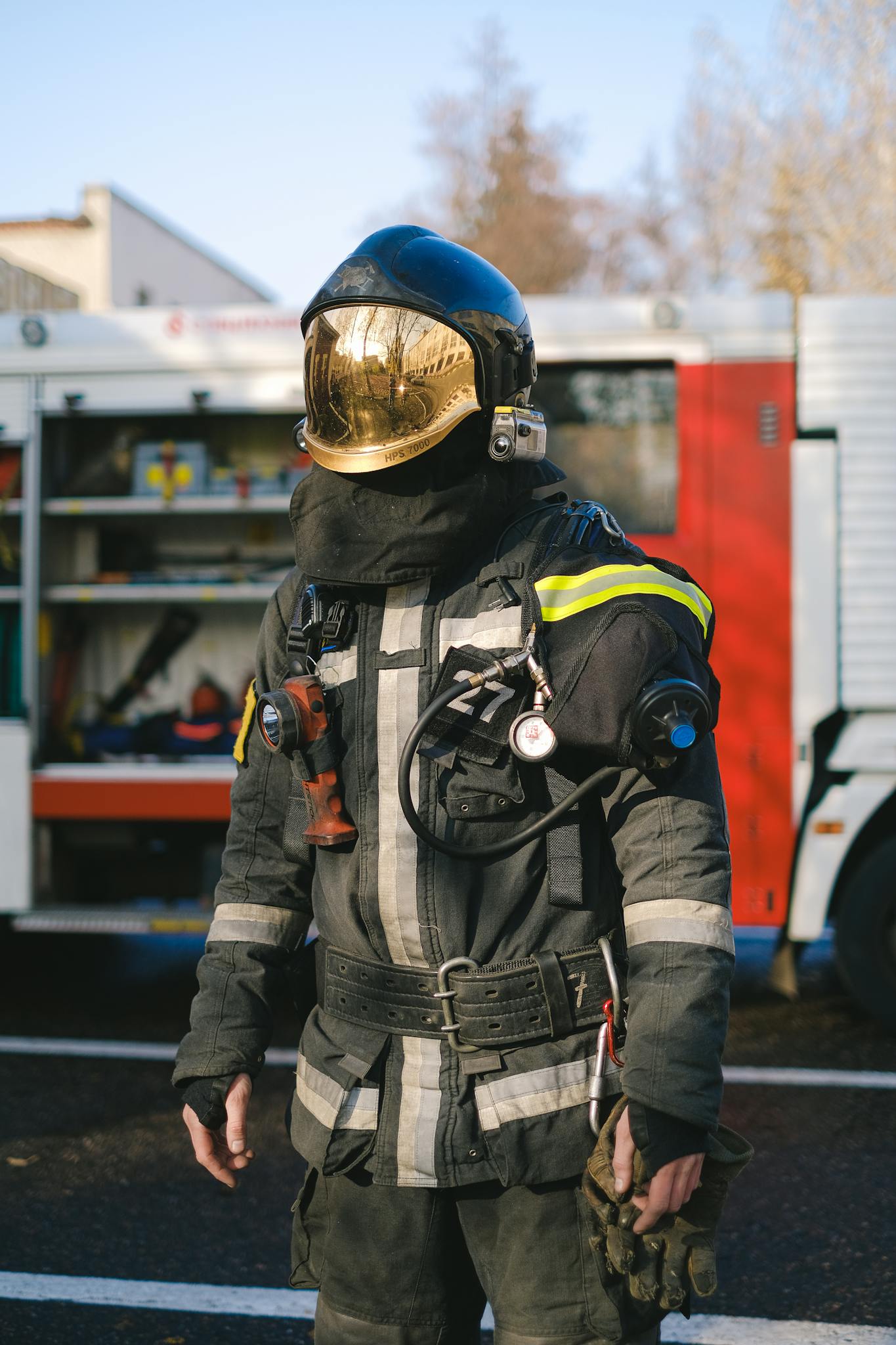 Firefighter in full protective gear standing beside a fire truck during daylight.